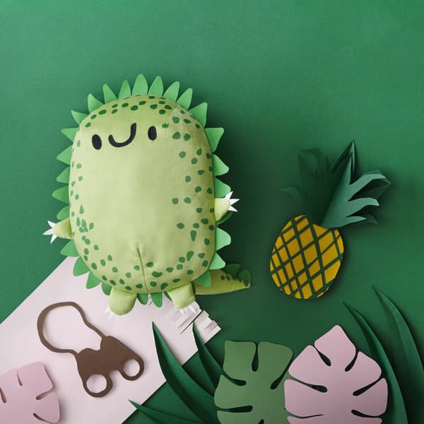 Peluche en forme de dinosaure vert dans un décor de jungle en papier.