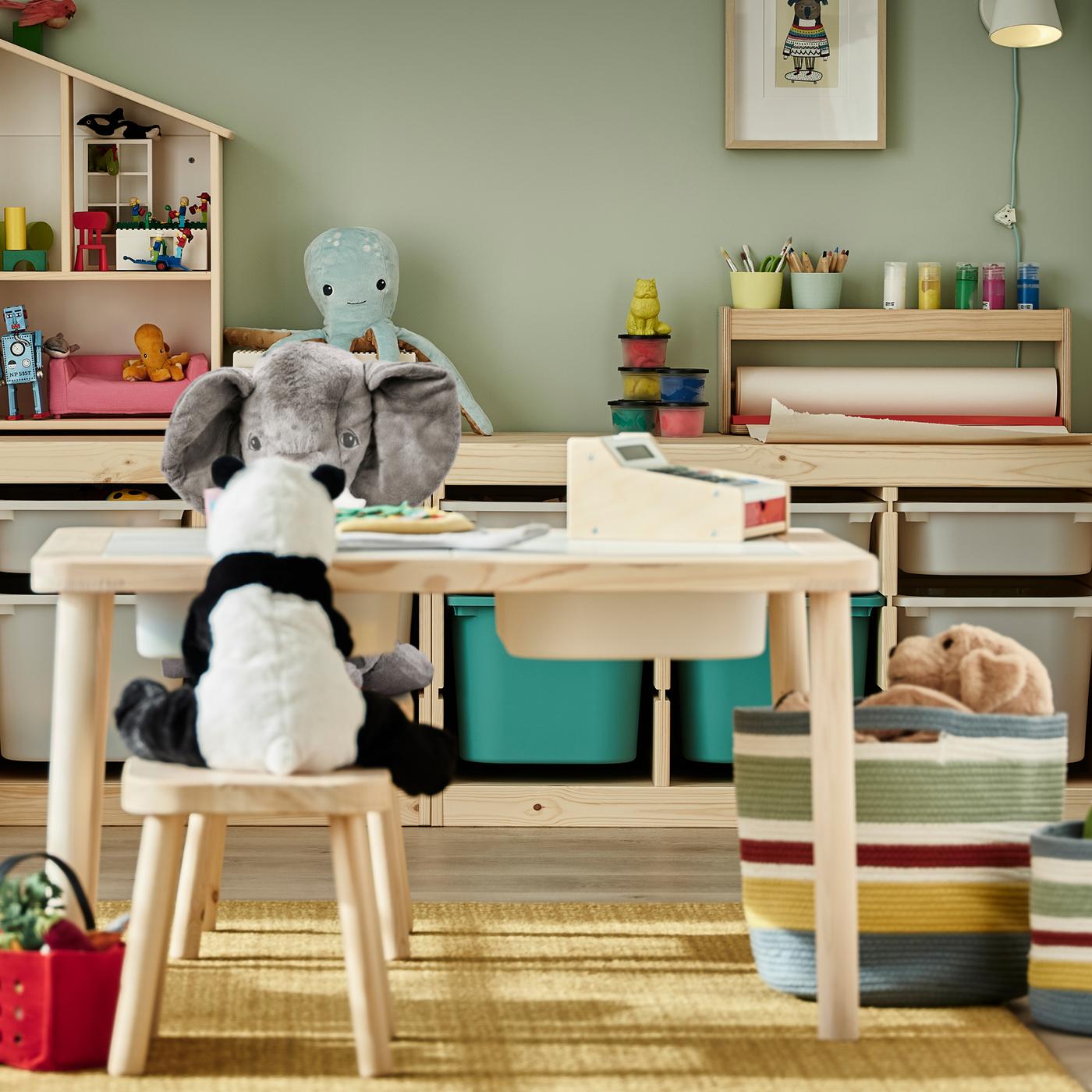 Peluches alrededor de una mesa infantil con taburetes de pino, y dos combinaciones de almacenaje con estructuras de pino que contienen juguetes.