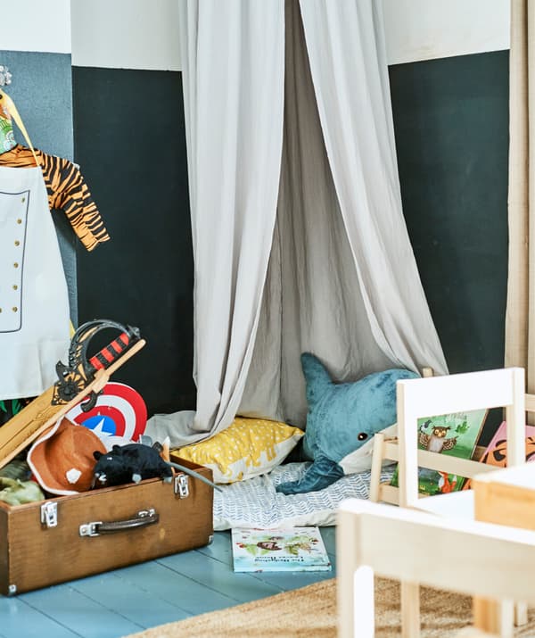 Peluches et coussins sous un ciel de lit à côté d'une valise remplie de jouets.