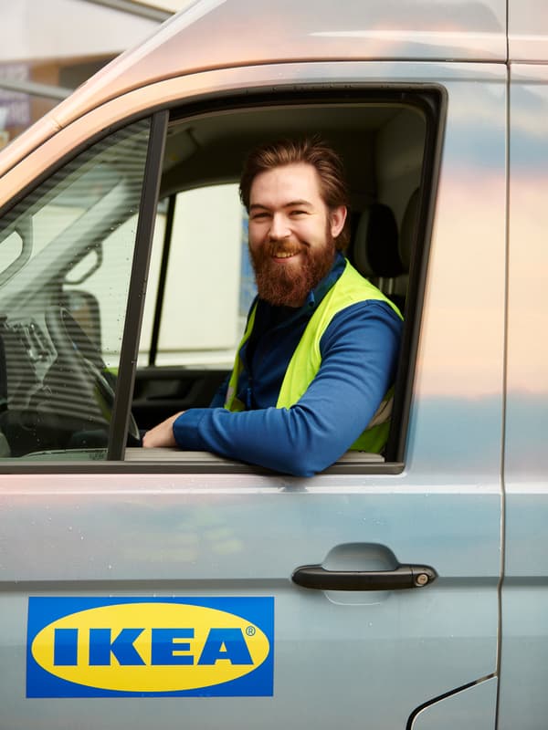Pemandu trak IKEA sedang duduk di belakang roda stereng dengan tingkap diturunkan dan sikunya diletakkan pada pintu.