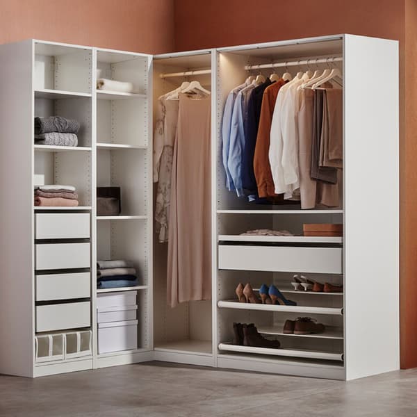 Penderie d'angle ouverte avec plusieurs optimisations de rangements et des vêtements accrochés à des ceintres.