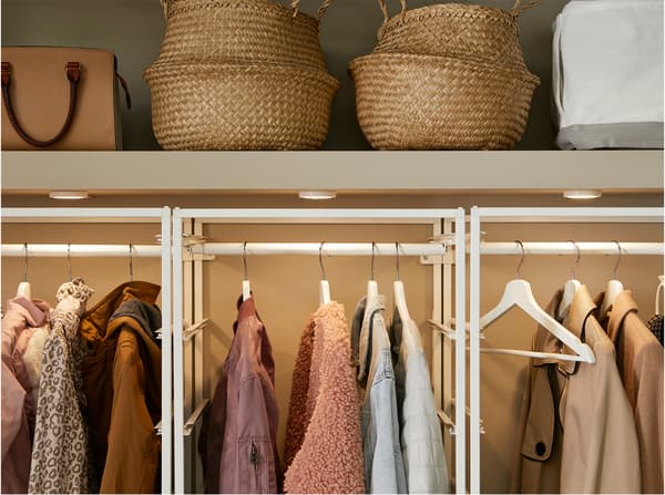 Penderie intégrée avec rangement modulaire JONAXEL en blanc, tringles à vêtements, éclairage et paniers en jonc de mer.