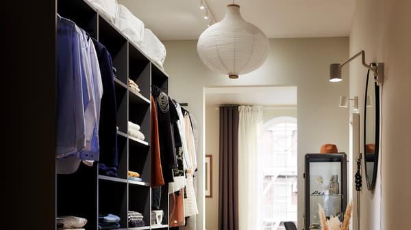 Penderie ouverte AURDAL avec vêtements pliés sur des étagères et suspendus à des tringles à habits, et des miroirs et lampes sur le mur opposé.
