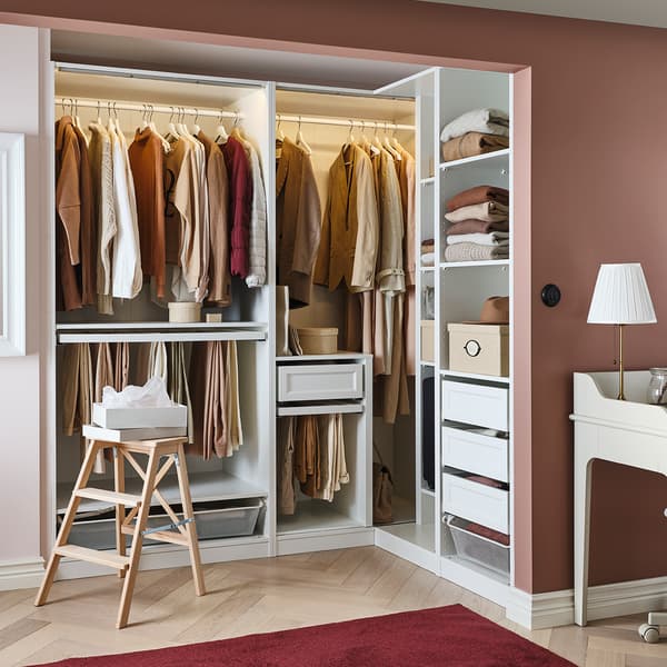 Penderie PAX blanche avec cintres, étagères, tiroirs et escabeau dans une chambre. 