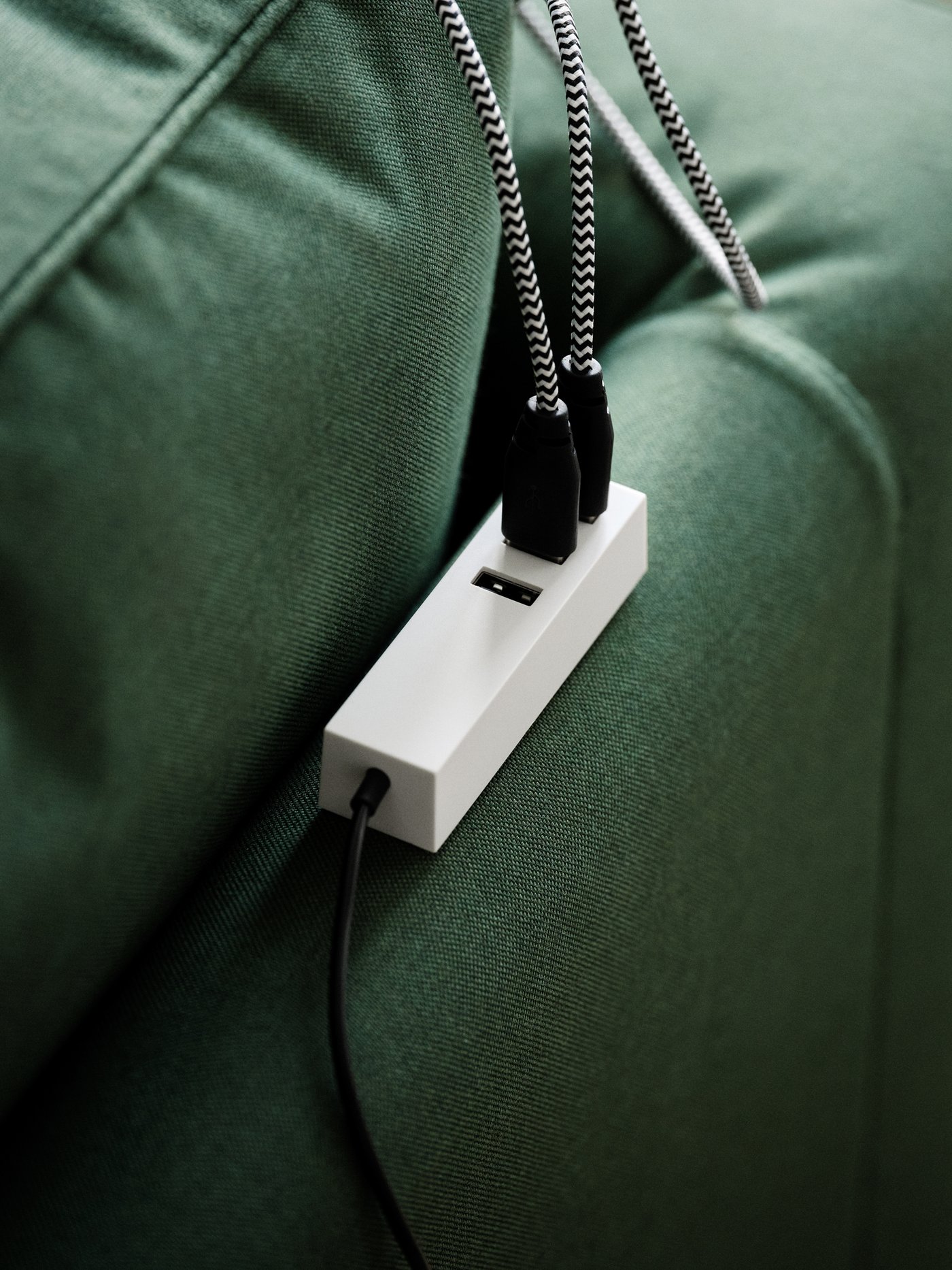 Pengecas USB bermagnet LÖRBY terletak di bahagian belakang sofa PÄRUP berwarna hijau dengan dua kabel disambungkan kepadanya.