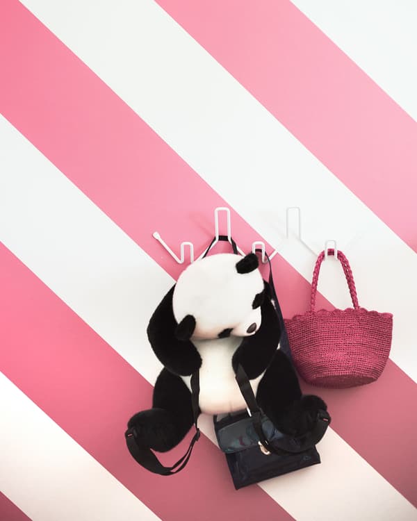 Penjador blanc muntat a una paret de ratlles roses i blanques, on pengen una bosseta de mà i un panda de peluix.