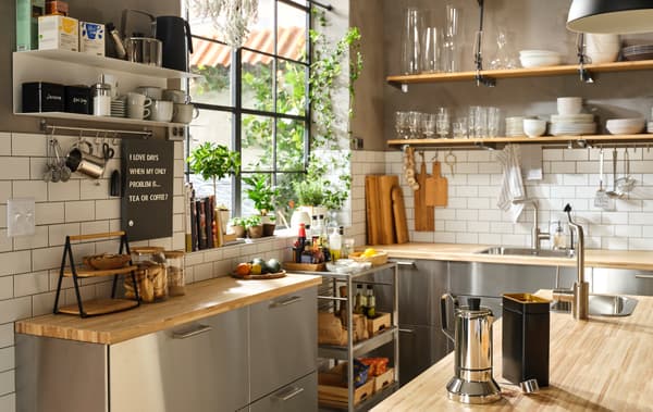 Penjuru dapur yang besar dengan tingkap yang besar, permukaan atas kerja dapur kayu, bahagian hadapan keluli tahan karat dan para terbuka untuk set makan malam.