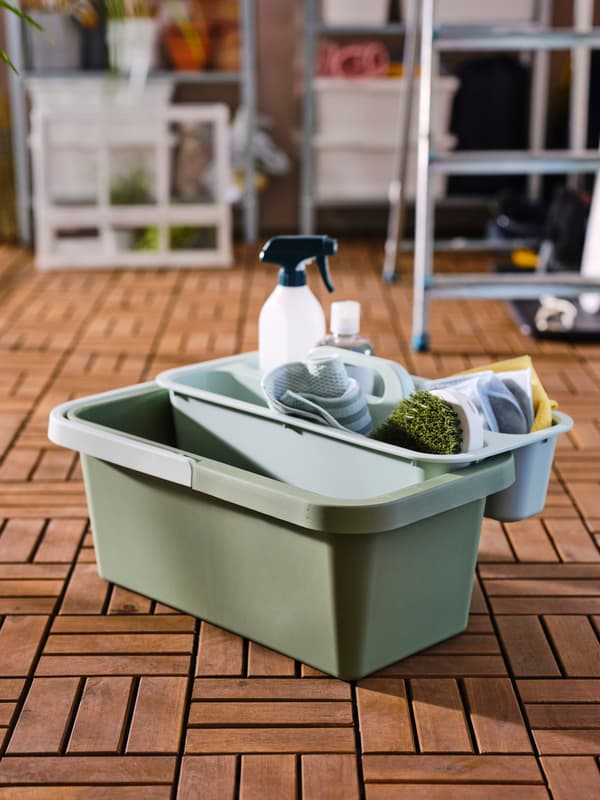 PEPPRIG green cleaning basket filled with PEPPRIG cleaning accessories is placed on the floor in front of the laundry area.