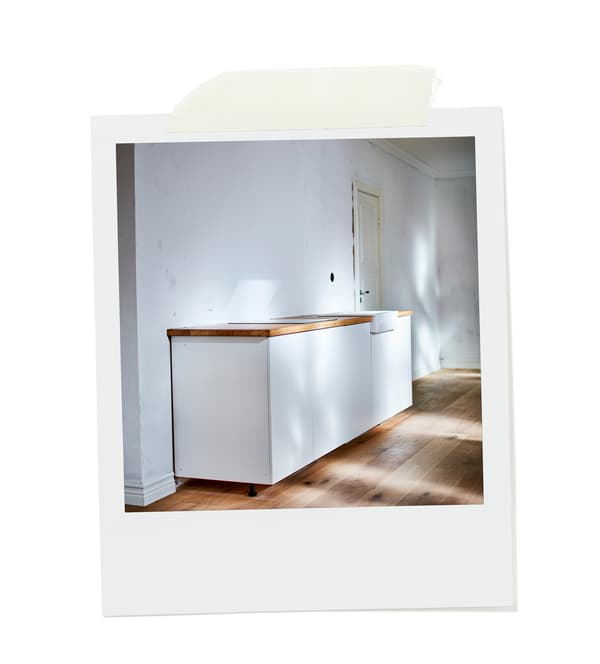 Pequena kitchenette branca em linha reta numa divisão vazia, com pavimento em madeira e paredes brancas.