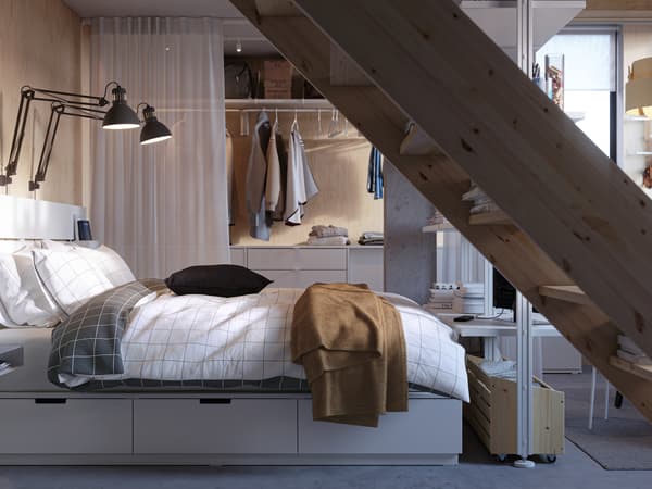 Pequeno quarto minimalista com estrutura de cama com arrumação NORDLI, cabeceira, e espaço de roupeiro separado por cortinados.