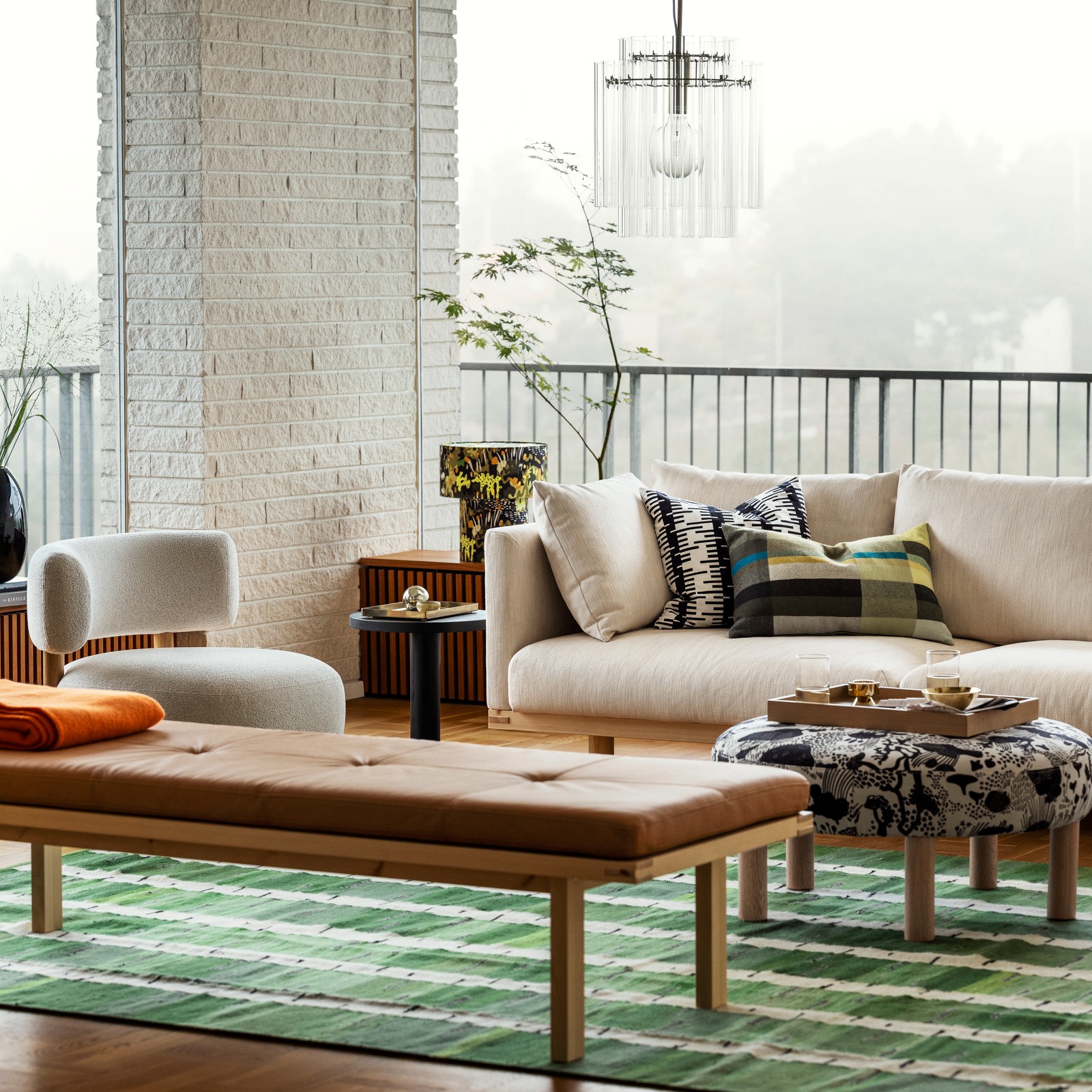 Perfect blend of Scandinavian aesthetics: light sofa, wood bench, round ottoman, green rug in an airy lounge