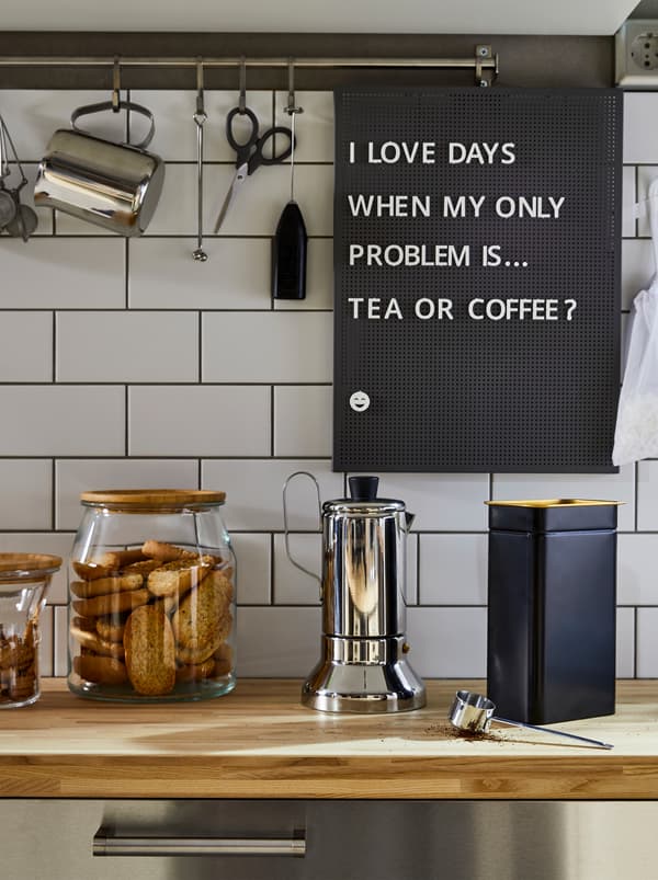 Permukaan atas kerja dapur yang mempunyai pembancuh kopi espreso METALLISK yang dibuat daripada keluli tahan karat, tin kopi BLOMNING berwarna biru dan balang kaca untuk biskut.