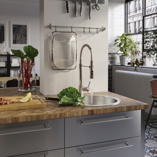 Permukaan atas kerja kayu, sink lekap pada permukaan atas kerja dan paip campuran dengan penyembur tangan. Penyembur tangan mencuci rubarb yang diletakkan di dalam sink lekap pada permukaan atas kerja.