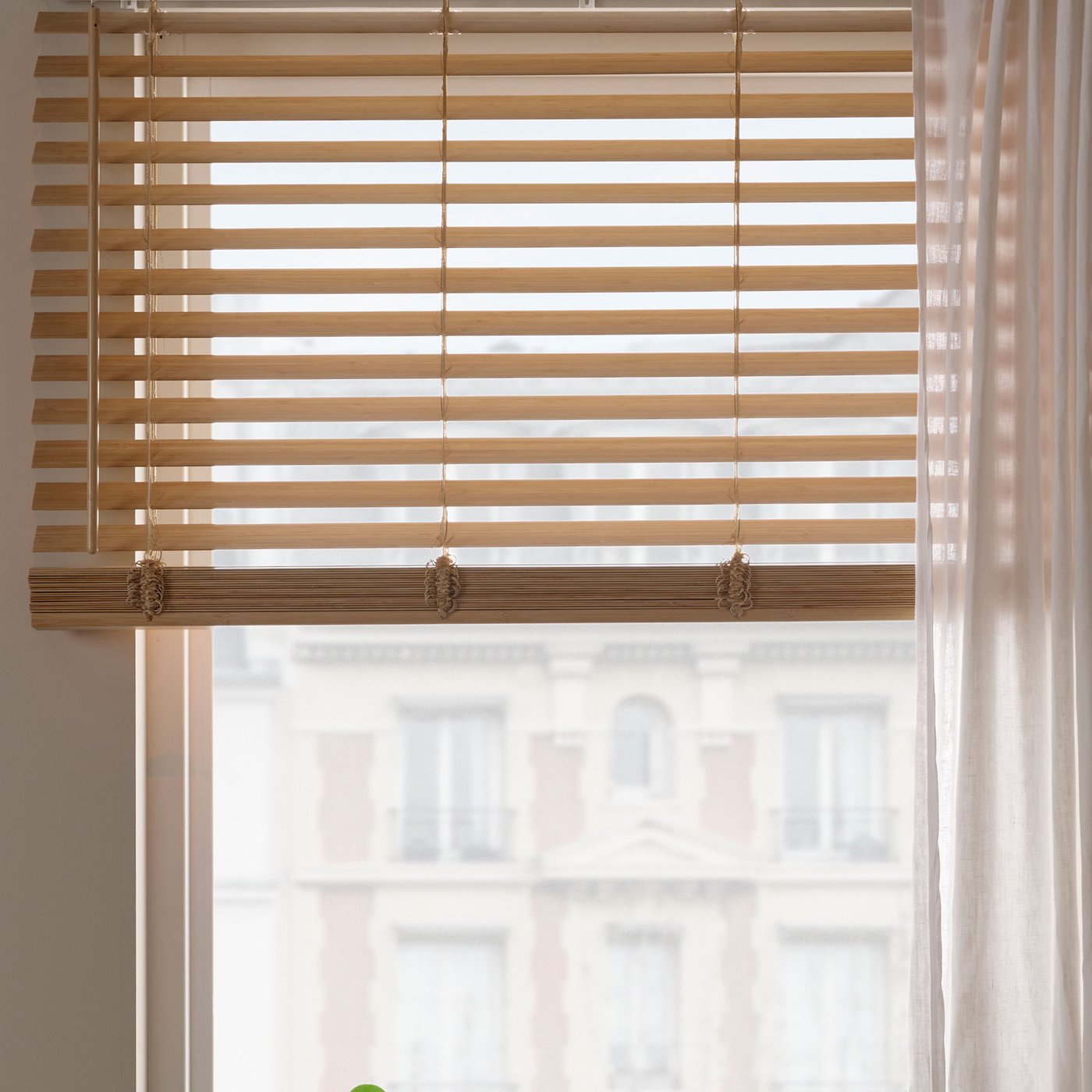 Persienner i bambu monterade i ett fönster, med mjukt dagsljus som filtreras in i rummet.
