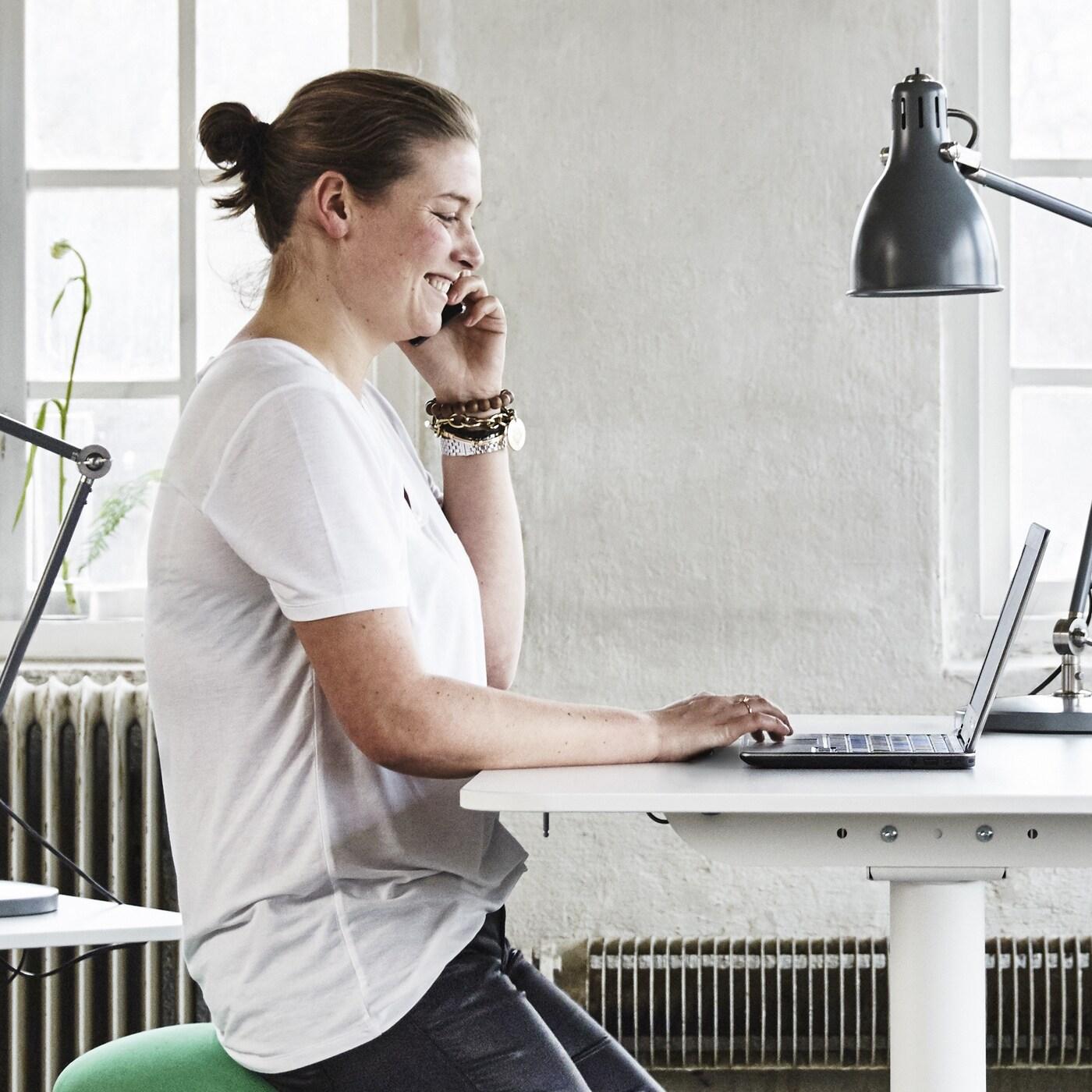 Person answering a call while working on a laptop in a bright environment, representing IKEA's telephone sales service.