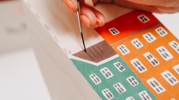 Person bemalt Häusermotiv auf dem KNUFF Zeitschriftensammler mit Farben.