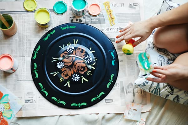Person decorating a dustbin lid with colours.