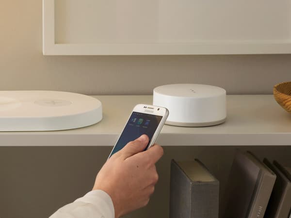 Person holding a smartphone connecting the IKEA Home smart app to the TRÅDFRI gateway, shown in a living room.