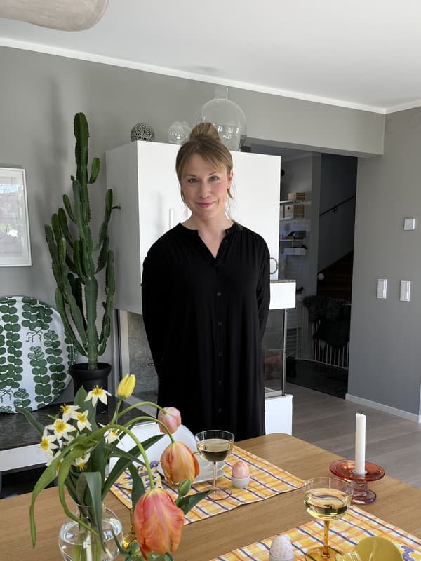 Person i modernt kök med dukat bord – blommor, glas med dryck, ljus och en kaktus i bakgrunden.