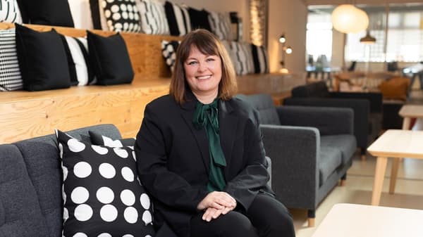 Person in a dark suit sitting on a sofa in a lounge area with monochrome patterned cushions and warm lighting in an IKEA store