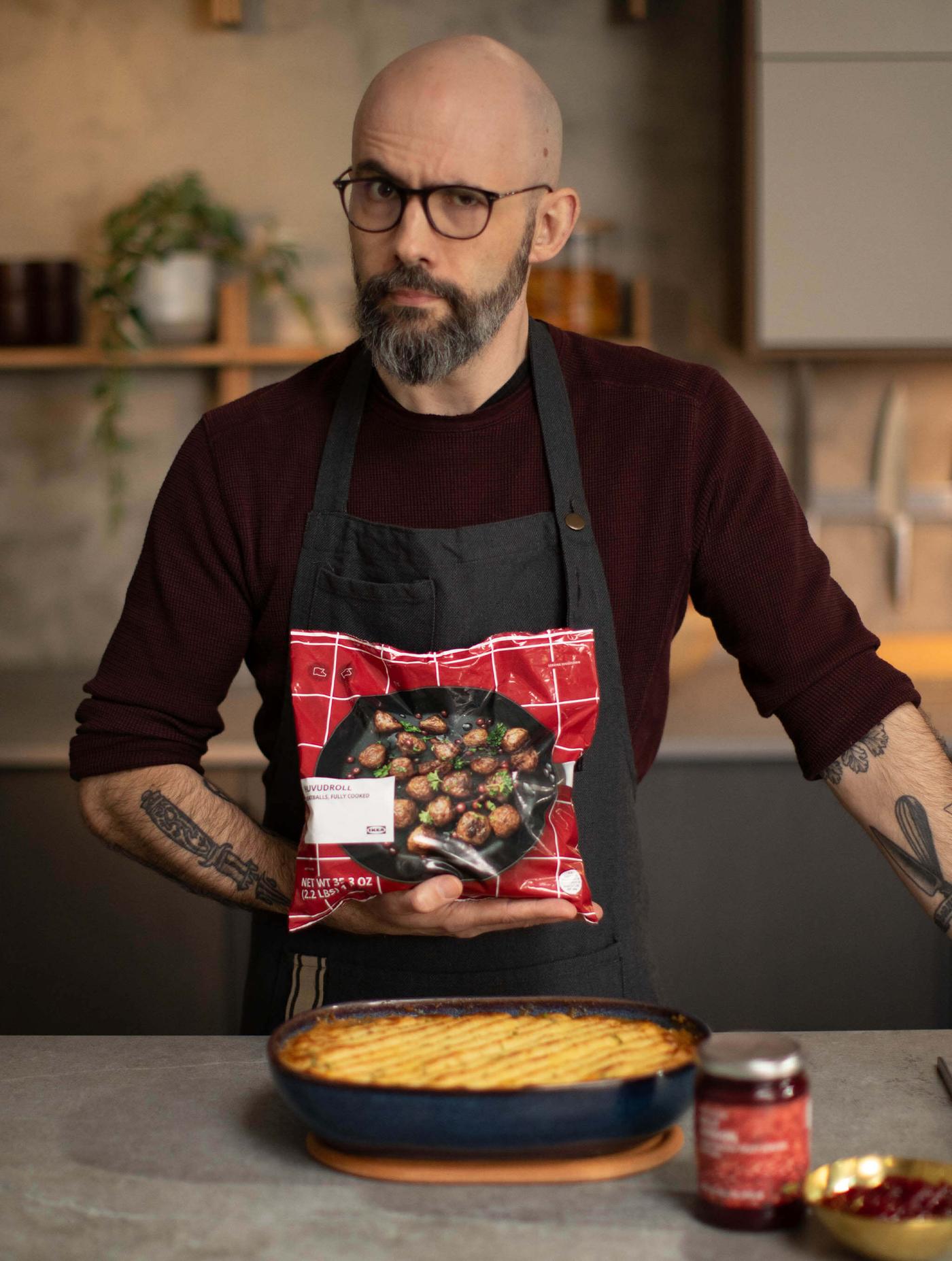 Person in a kitchen holding a food package above a baked dish on the counter.