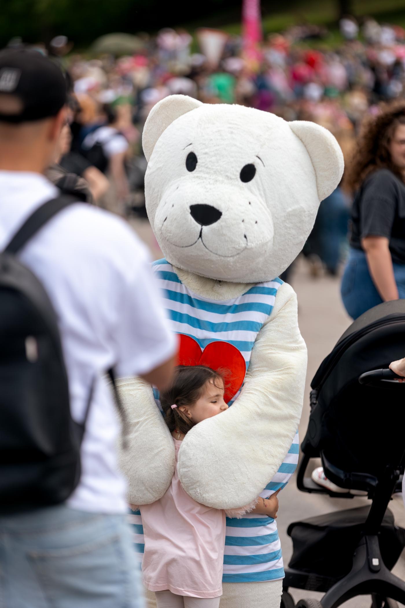 Person in a Teddy Bear costume interacting with visitors at a crowded festival, creating a fun and playful atmosphere.