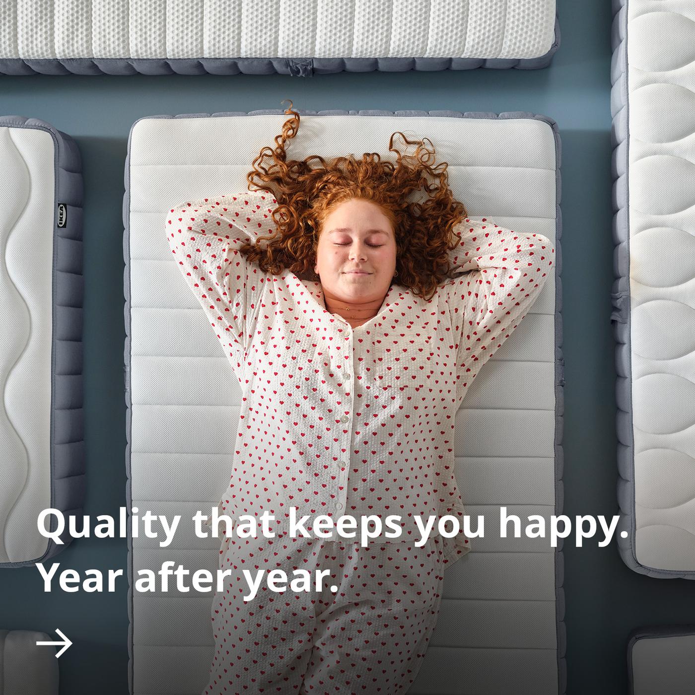 Person in patterned pyjamas lying on a mattress with arms behind the head, viewed from above and surrounded by other mattresses.