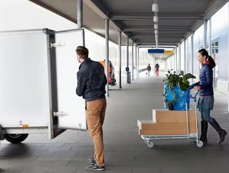 Person lastar av från transportvagn medan en annan person kör en vagn med kartonger i en täckt gång.