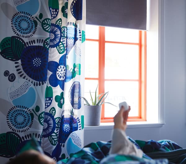 Person opening smart blinds FYRTUR from bed with a remote control device.
