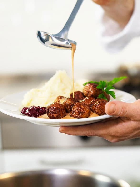 Person pouring gravy over meatballs and mash