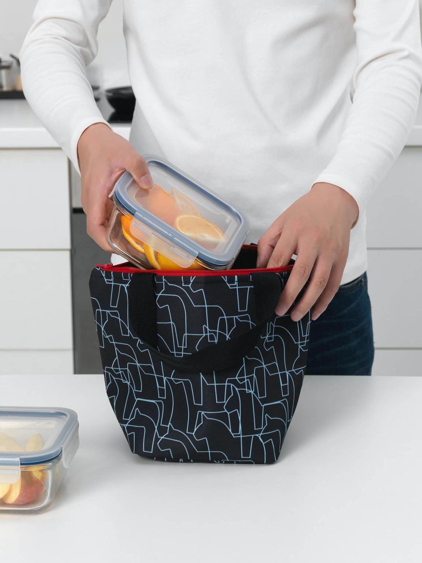 Person putting a container of food in a HÄSTHAGE lunch bag.
