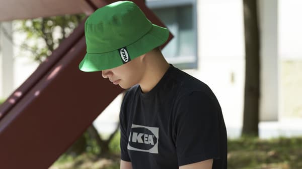 Person sitting outdoors wearing a green bucket hat and black IKEA t-shirt