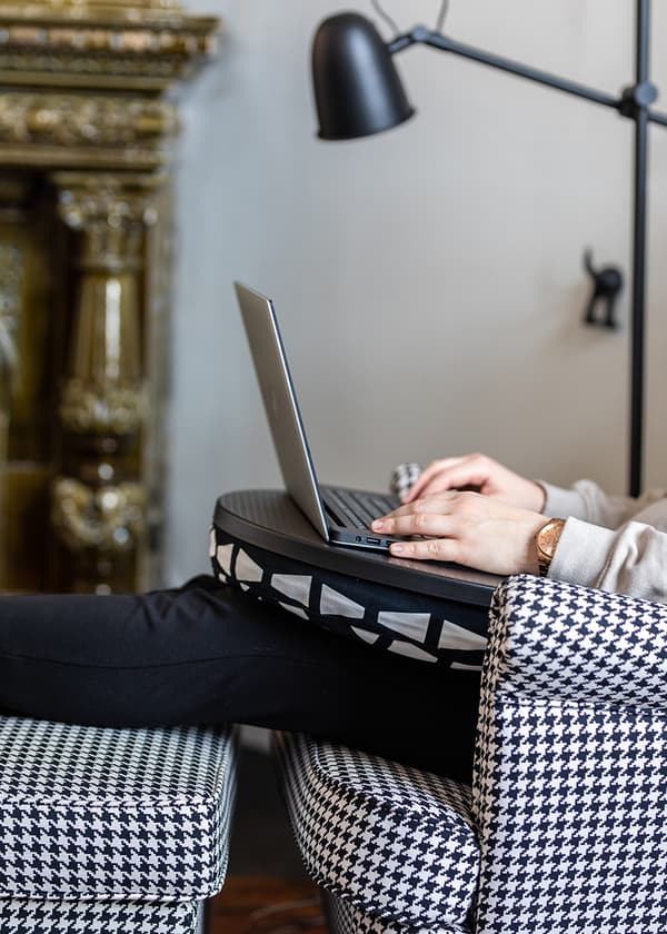 Person som sitter i en STRANDMON fåtölj med hundtandsmönster, använder en laptop i knät och vilar fötterna på en fotpall.