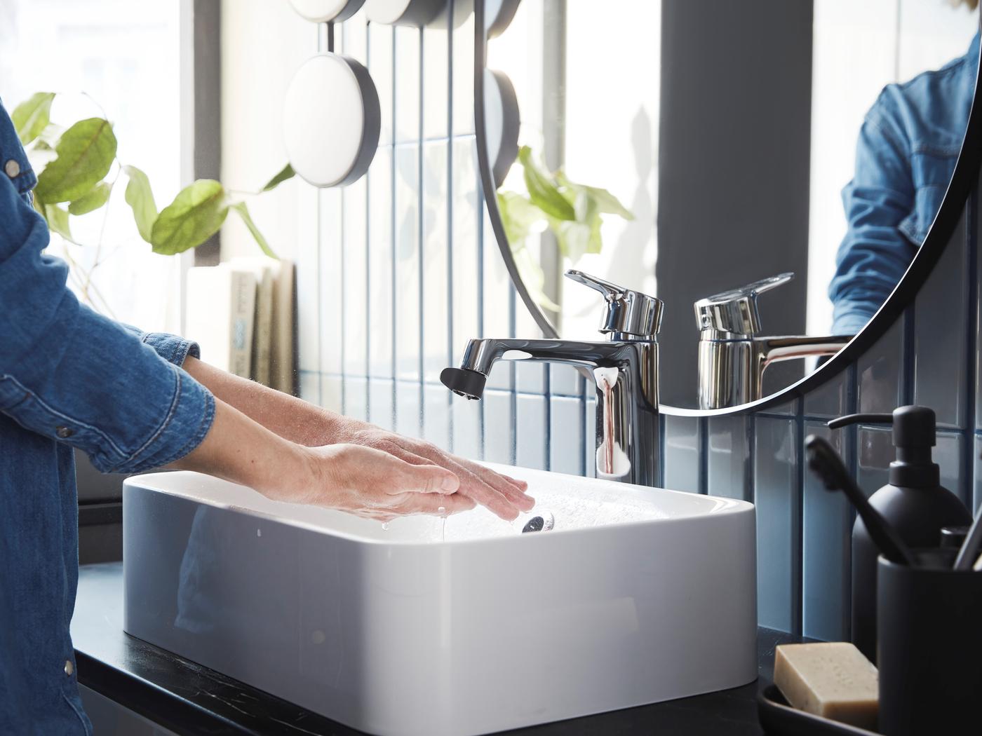 Person wäscht sich die Hände an einem modernen IKEA-Waschbecken mit verchromter Armatur im stilvoll eingerichteten Badezimmer.