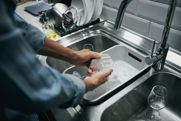 Person washing dishes in a grey GRUNDVATTNET rinsing tub.