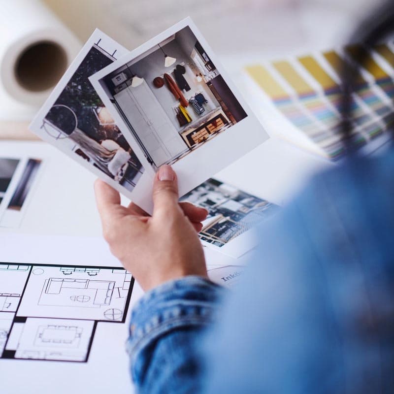 Persona con due foto, una mostra un interno; sul tavolo campioni di colore e planimetrie.