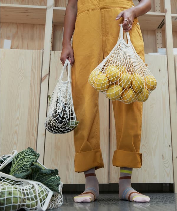 Personne en salopette jaune portant des sacs de fruits et de légumes.
