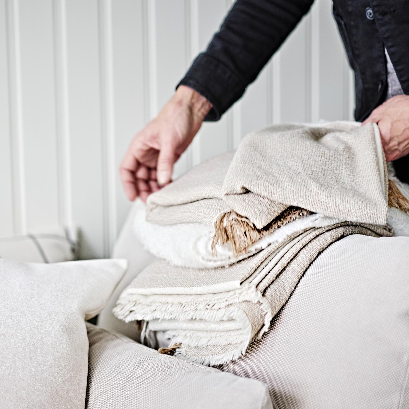 Personne pliant un plaid GUNNEMOR gris-beige sur l’accoudoir d’un module d’angle 1 place SÖDERHAMN en beige clair.