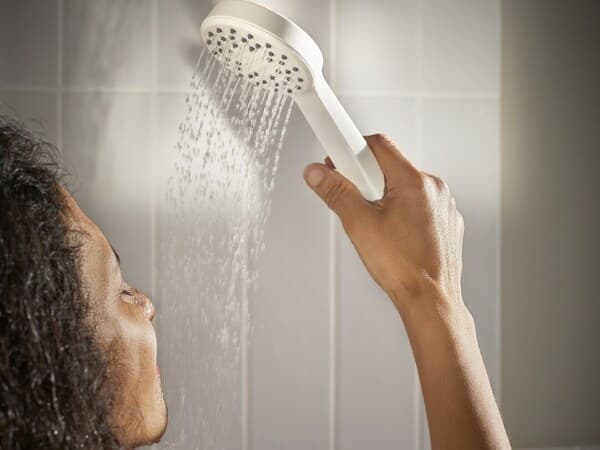 Personne se versant de l'eau sur la figure avec un pommeau de douche.