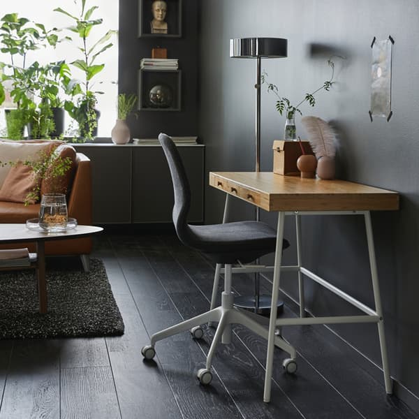 Petit bureau avec dessus en bambou et pieds blancs, adossé au mur gris foncé du salon.