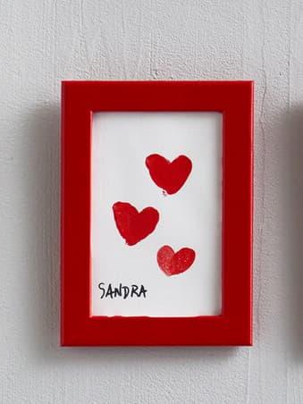 Petit cadre FIKSBO avec des bords rouges ,sur un mur blanc, contenant une peinture avec trois coeurs rouges et le prénom Sandra écrit en bas à gauche sur un fond blanc.