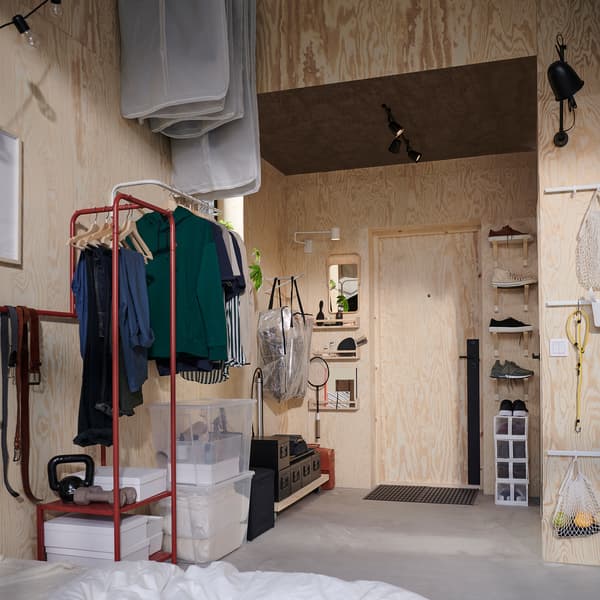 Petit hall d’entrée aux murs hauts. Des tringles à vêtements et des consoles sont installées verticalement pour gagner de la place.