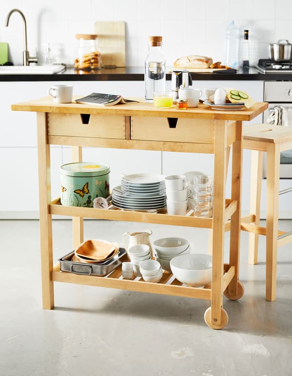 Petit îlot de cuisine en bois avec aliments pour le petit déjeuner et vaisselle rangée sur les tablettes du bas.
