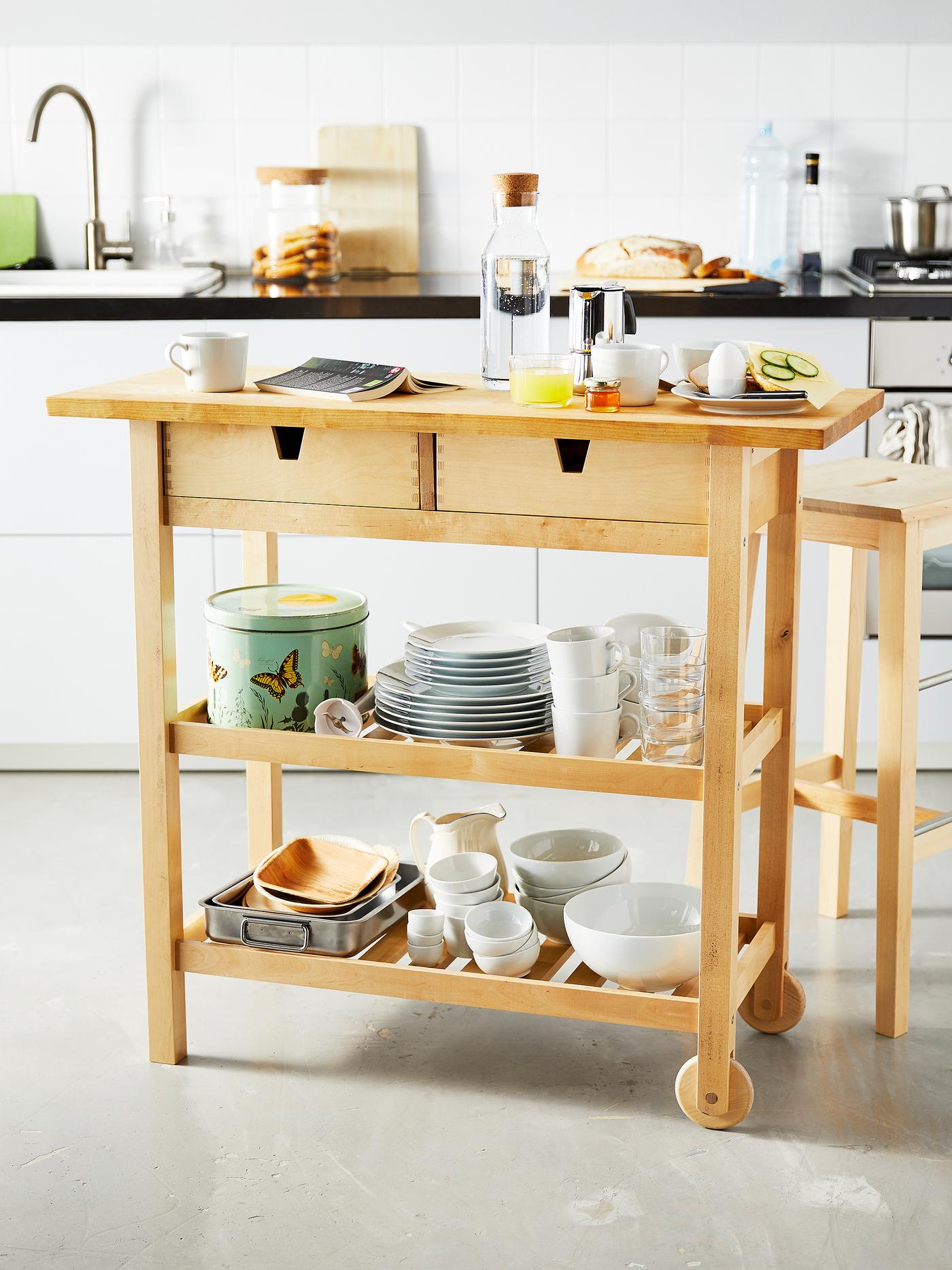 Petit îlot de cuisine en bois avec aliments pour le petit déjeuner et vaisselle rangée sur les tablettes du bas.
