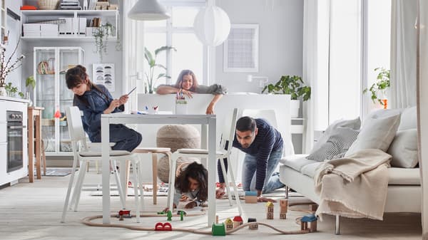Petit intérieur où une famille joue avec un train LILLABO disposé dans une pièce avec un lit, un canapé, une table, une kitchenette et des rangements.