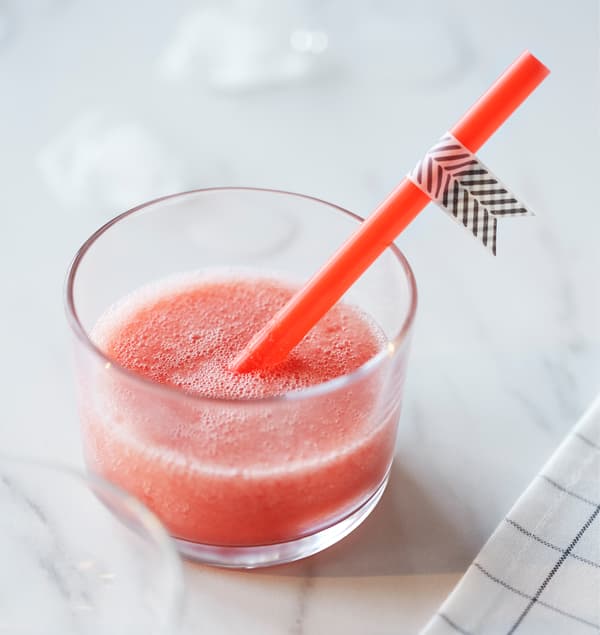 Petit verre avec paille, rempli de smoothie rouge.
