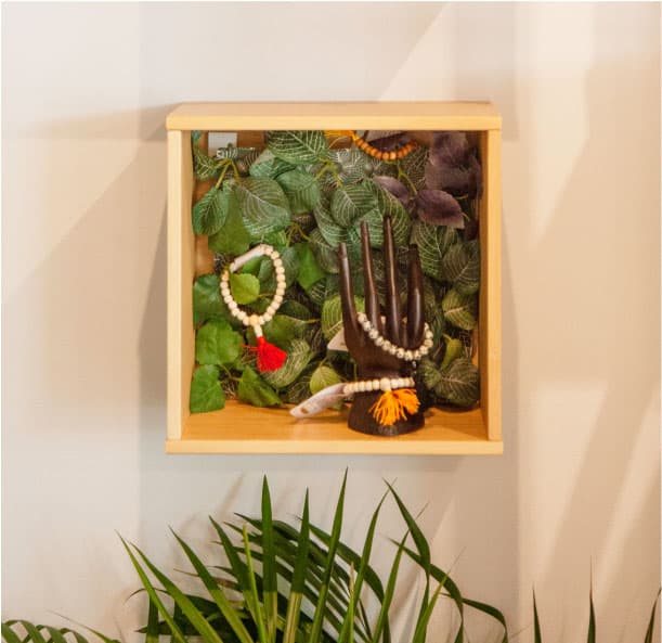 Petita vitrina decorativa amb fons de fulles verdes i joies artesanals exposades amb un suport en forma de mà.