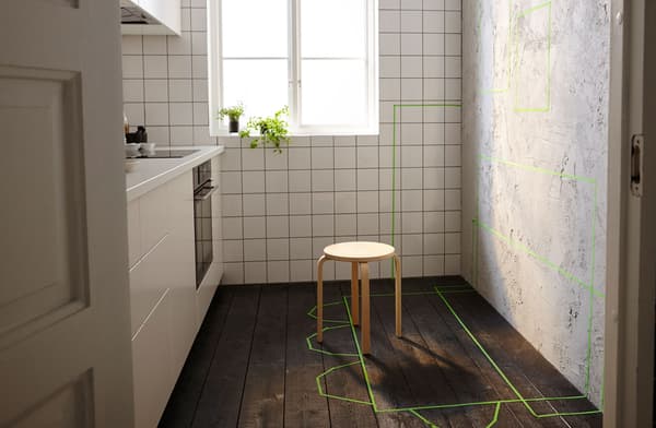 Petite cuisine avec mur libre d’un côté, marquages à l’adhésif vert à l’emplacement des futurs rangements, tables et chaises.