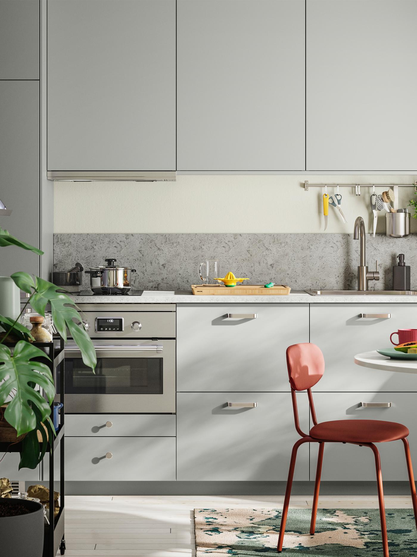 Petite cuisine linéaire avec façades HAVSTORP gris clair, petit coin repas et plante verte au premier plan.