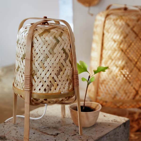 Petite lampe de table KNIXHULT tissée en bambou, avec le lampadaire KNIXHULT correspondant en arrière-plan.